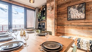 A dining area with a wooden table set for four, large windows with a mountain view, and a rustic wall with a polar bear painting.