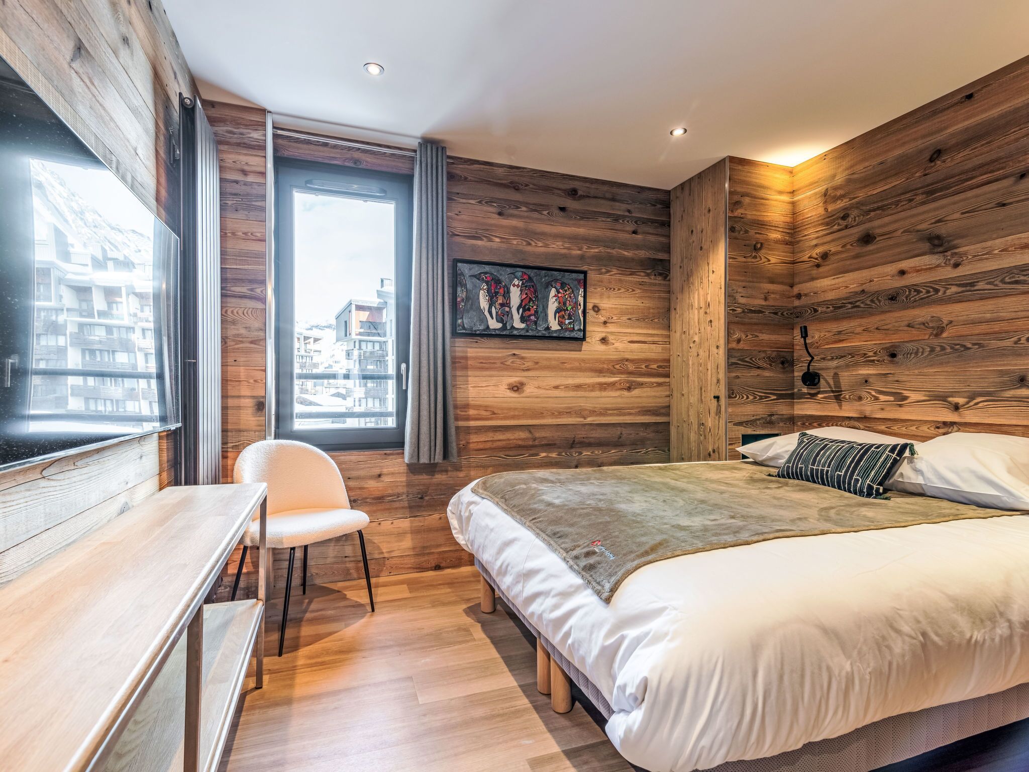 Un dormitorio con pared de madera, una cama, un escritorio y una silla.