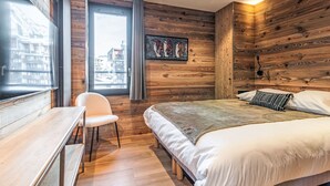 A bedroom with a wooden wall, a bed, a desk, and a chair.