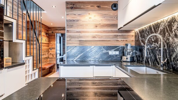 A modern kitchen with wooden accents, a marble backsplash, and a sleek black countertop.