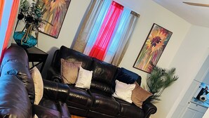 A living room with a black leather sofa, a coffee table, and two paintings on the wall. - Charming 3-bedroom house in beautiful Jacksonville With WiFI & workspace. (Jacksonville)