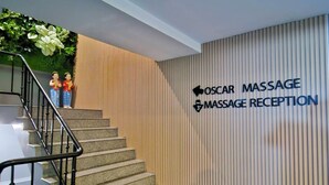 Ein Empfangsbereich mit einem Schild für 'OSCAR MASSAGE RECEPTION' und einer Treppe, die zu einer oberen Etage führt.
