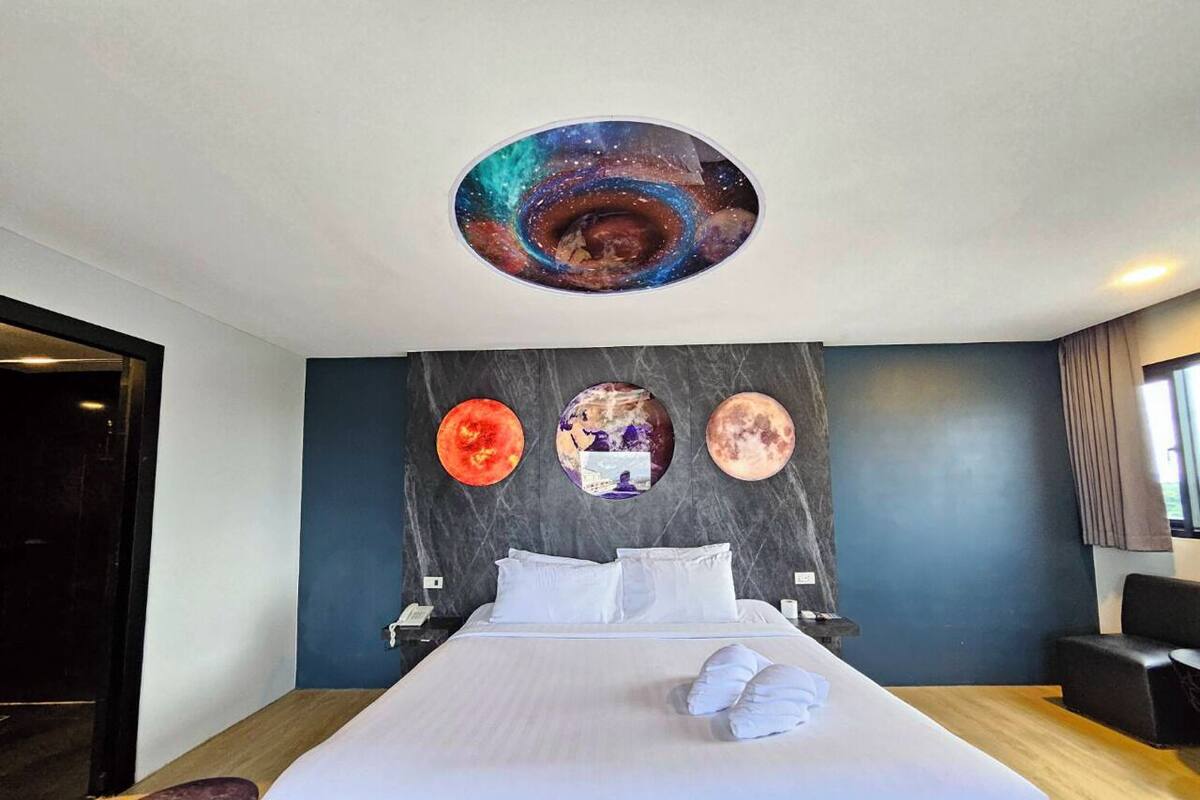 Une chambre d’hôtel avec un grand lit, un plafond décoré sur le thème de la galaxie et trois œuvres d’art murales représentant des planètes.