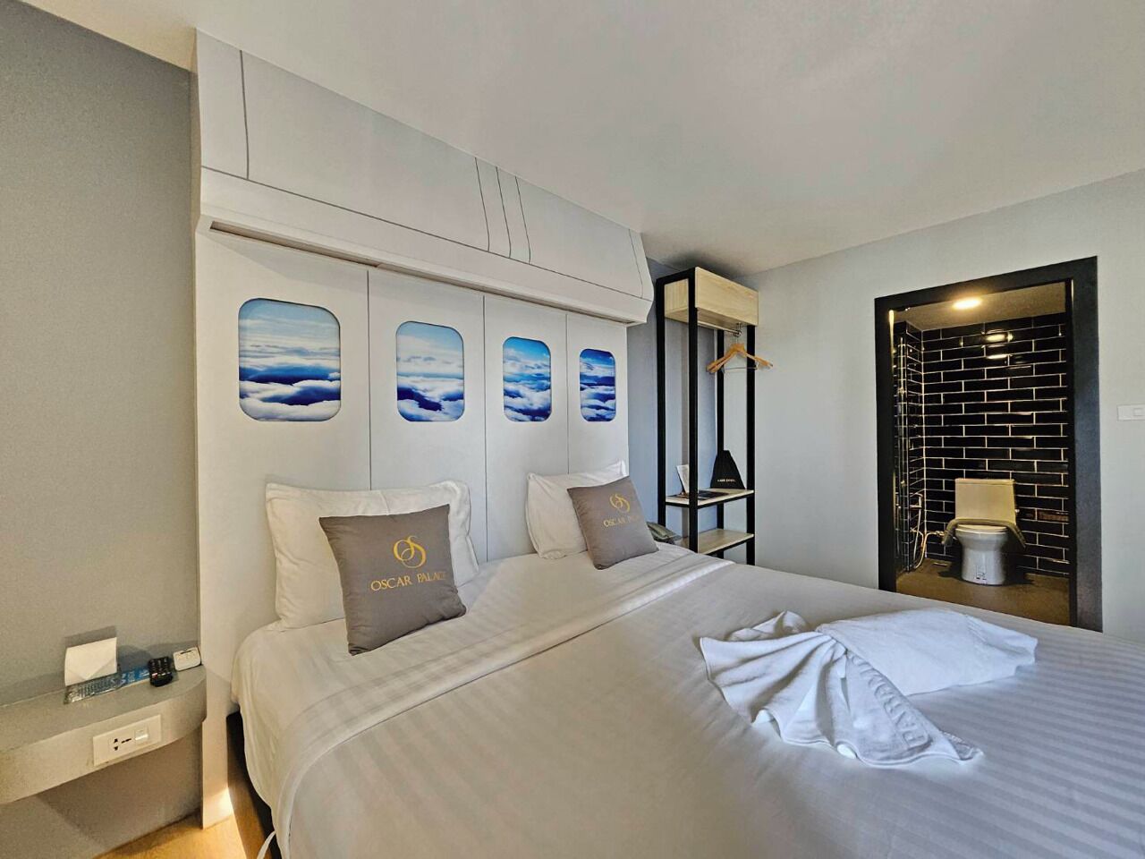 A hotel room with a large bed, a nightstand, a mirror, and a view of the bathroom through a glass partition.