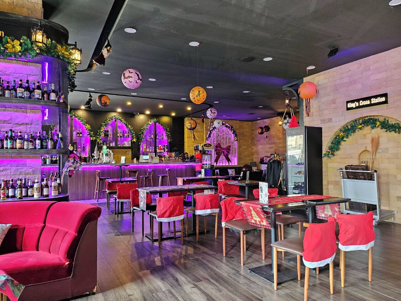 Un área de bar con varias mesas y sillas, una barra con botellas y una pared decorativa con un letrero que dice "King's Cross Station".