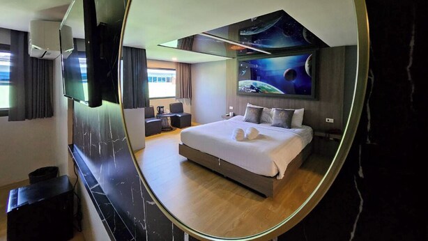 Ein modernes Hotelzimmer mit einem großen Bett, einem Wand-Fernseher und einem Wandgemälde zum Thema Weltraum.