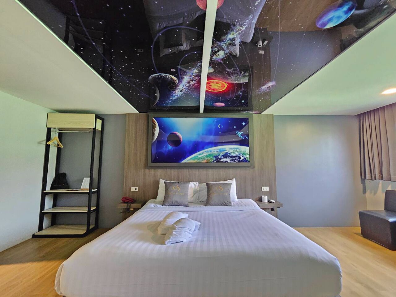 A hotel room with a large bed, a wall-mounted shelf, and a ceiling mural depicting space.