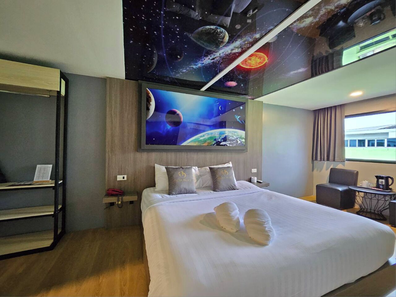 A hotel room with a large bed, a desk, a chair, a bookshelf, and a wall mural of space.