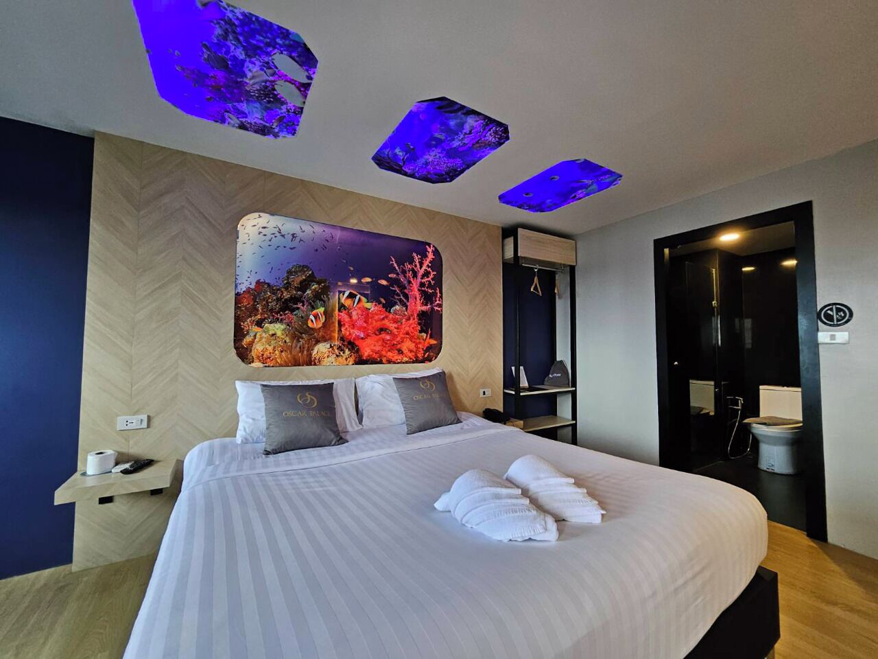 A modern hotel room with a large bed, a nightstand, a wall-mounted TV, and a bathroom visible through an open door.