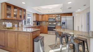 Una cocina moderna con armarios de madera, encimeras de granito, electrodomésticos de acero inoxidable y una isla central con taburetes de bar.
