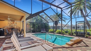 Una piscina interior con sillones de descanso, una chimenea de piedra y vistas a palmeras y casas.