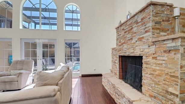 Amplia sala de estar con chimenea de piedra, ventanas arqueadas y vista a una piscina.