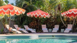 A pool area with lounge chairs and red umbrellas. - Beach Oasis: Hot tub, Pool, Mini-golf, Game Room (Seminole)