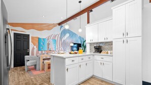 A modern kitchen with white cabinetry, a wooden floor, and a colorful mural on the wall. - Beach Oasis: Hot tub, Pool, Mini-golf, Game Room (Seminole)