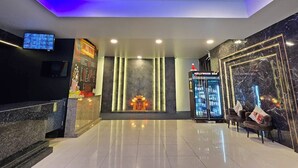 A lobby with a reception desk, a television, a decorative wall, a bar area, and seating. - Hollywood Dannok Hotel (Sadao)