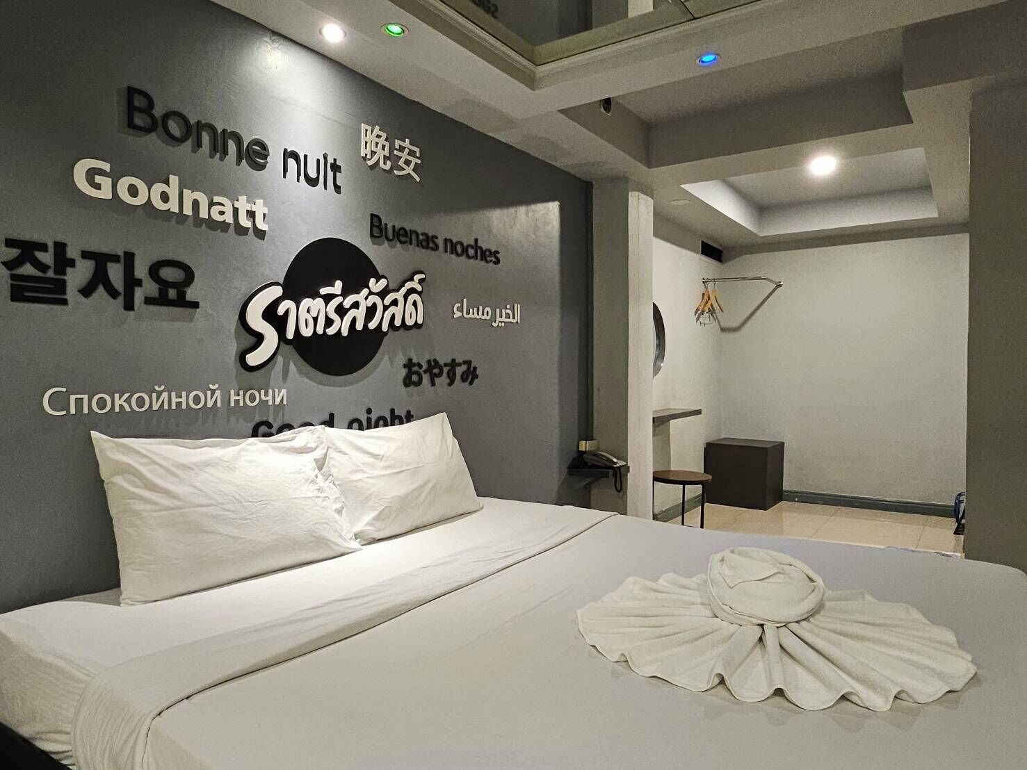 A hotel room with a bed, a wall with multilingual text, a small table, and a chair.