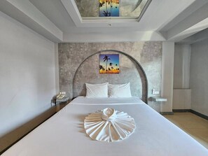 A hotel room with a large bed, a curved headboard, a painting of palm trees, and a skylight. - Hollywood Dannok Hotel (Sadao)