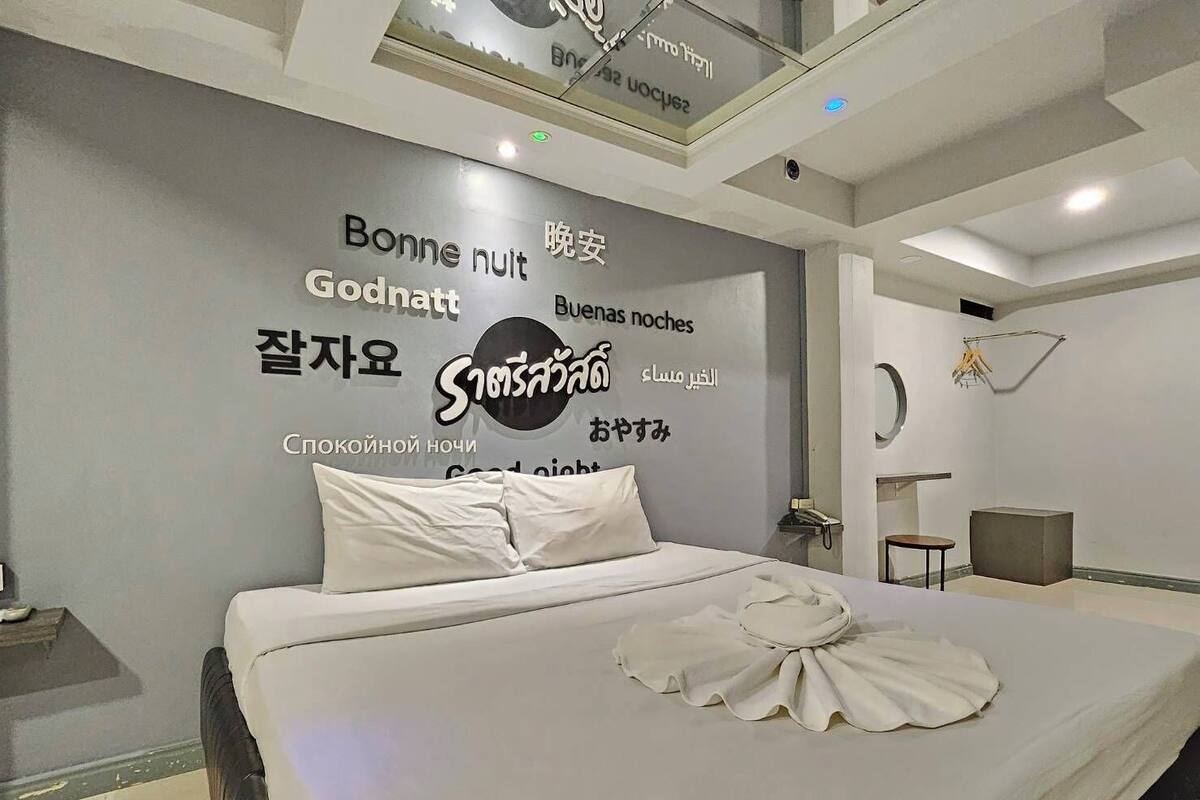 A modern hotel room with a large bed, a wall-mounted TV, and a small bedside table.