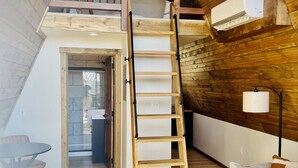 Un espacio tipo loft con una escalera de madera que lleva a un nivel superior, un pequeño comedor y una zona de estar acogedora con sofá y cojines.
