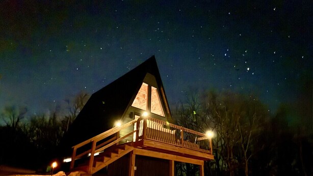 Una cabaña con balcón, escaleras de madera y un cielo nocturno estrellado.
