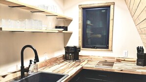 Una cocina moderna con encimera de madera, armarios negros, un lavabo negro y una ventana sobre el lavabo.
