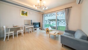 Een moderne woonkamer met een grijze bank, een eettafel met stoelen, een televisie en een klein hondenhuis.