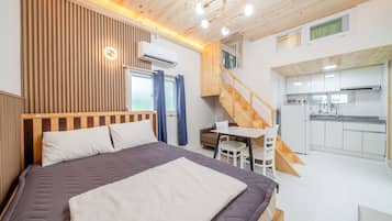 Un dormitorio con cama, mesita de noche, una silla, ventana con cortinas y una escalera que lleva a una zona de cocina.