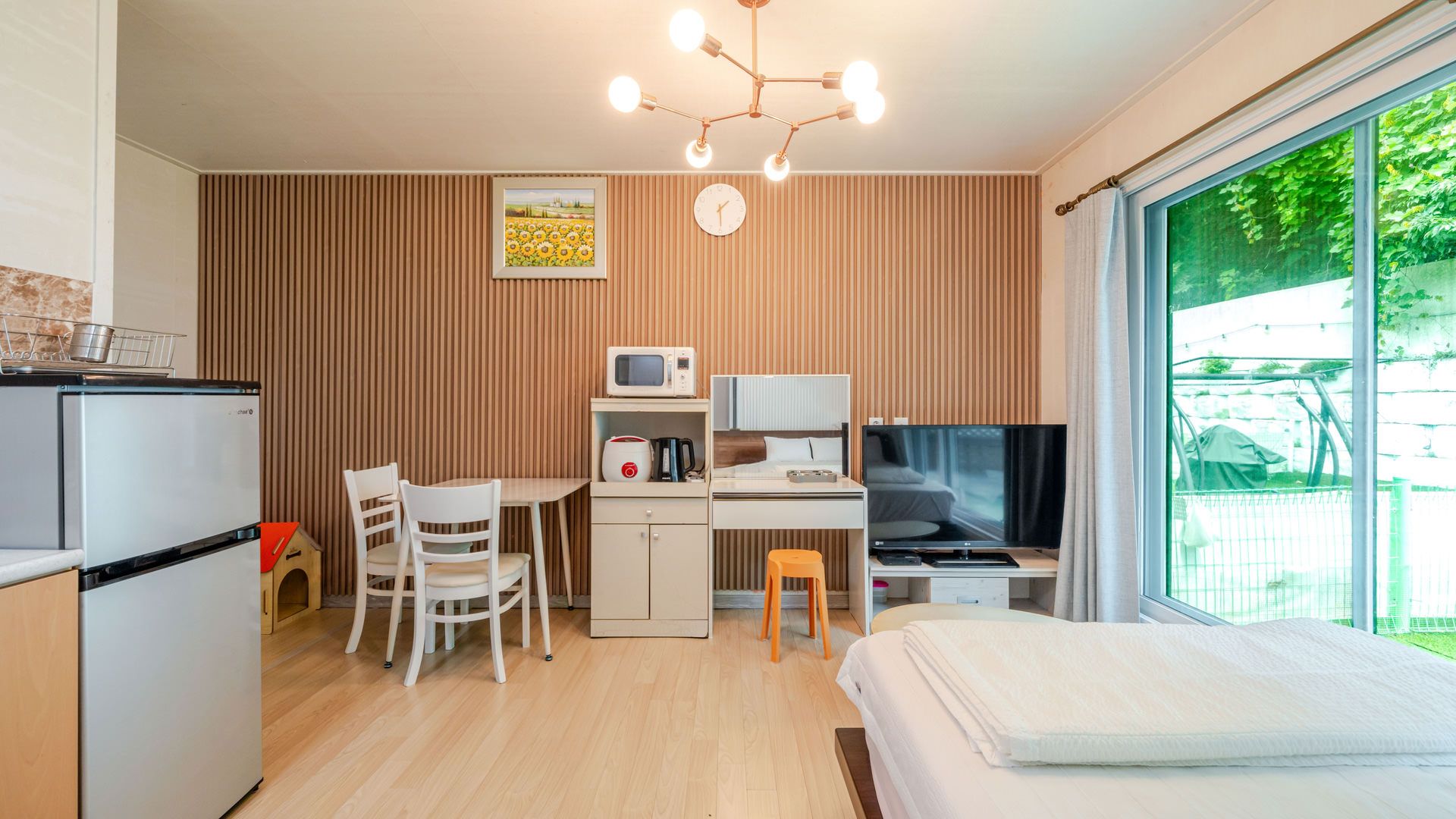 Ein kompaktes Hotelzimmer mit Küchenzeile, Essbereich, einem Bett und einem großen Fenster mit Blick ins Freie.
