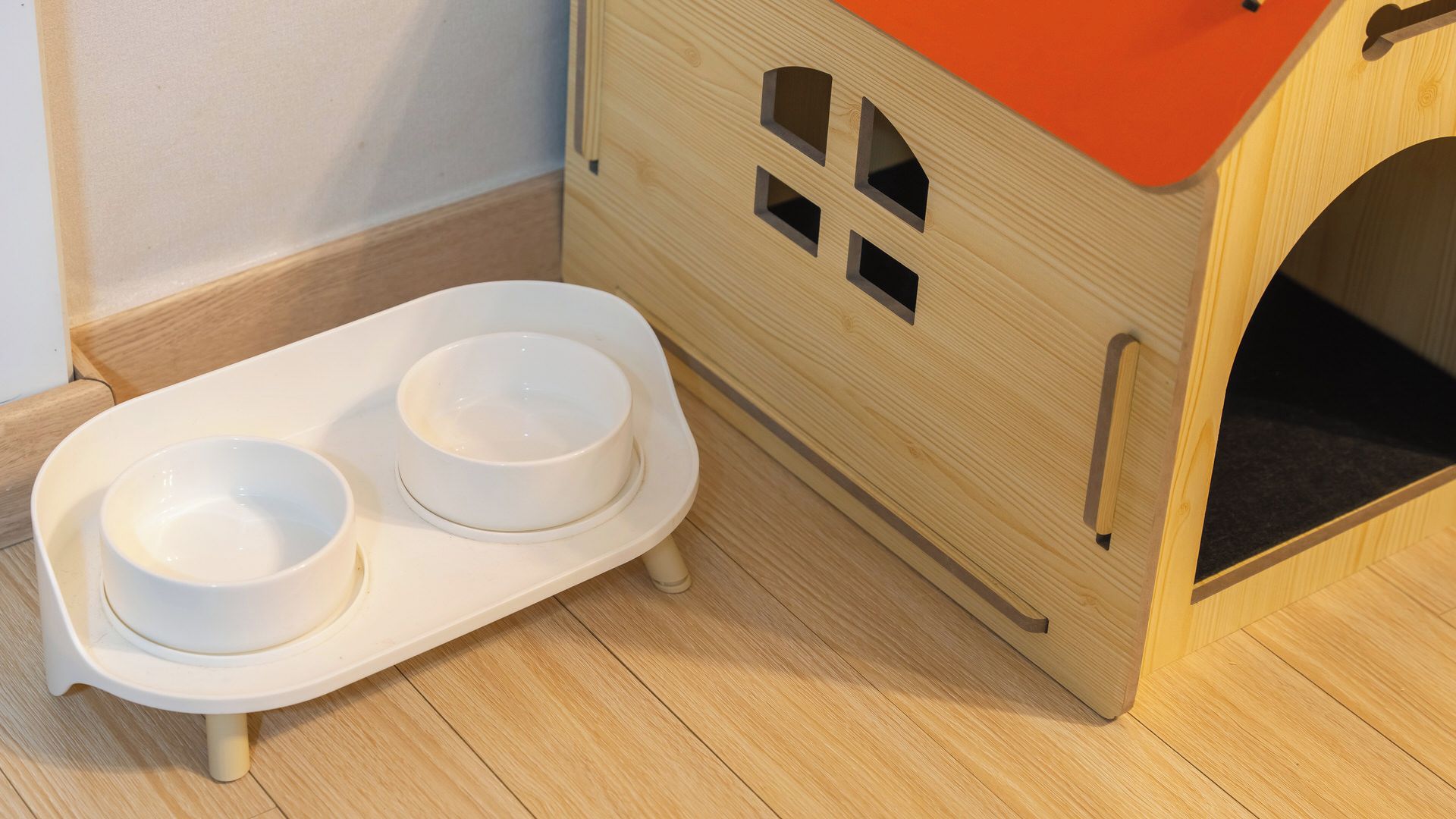 Una cama de madera para mascotas con parte superior roja y un plato de alimentación blanco con dos cuencos.
