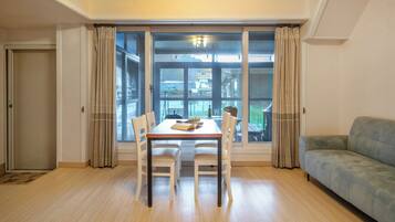 Un comedor con una mesa y sillas, un sofá y ventanas grandes con cortinas.