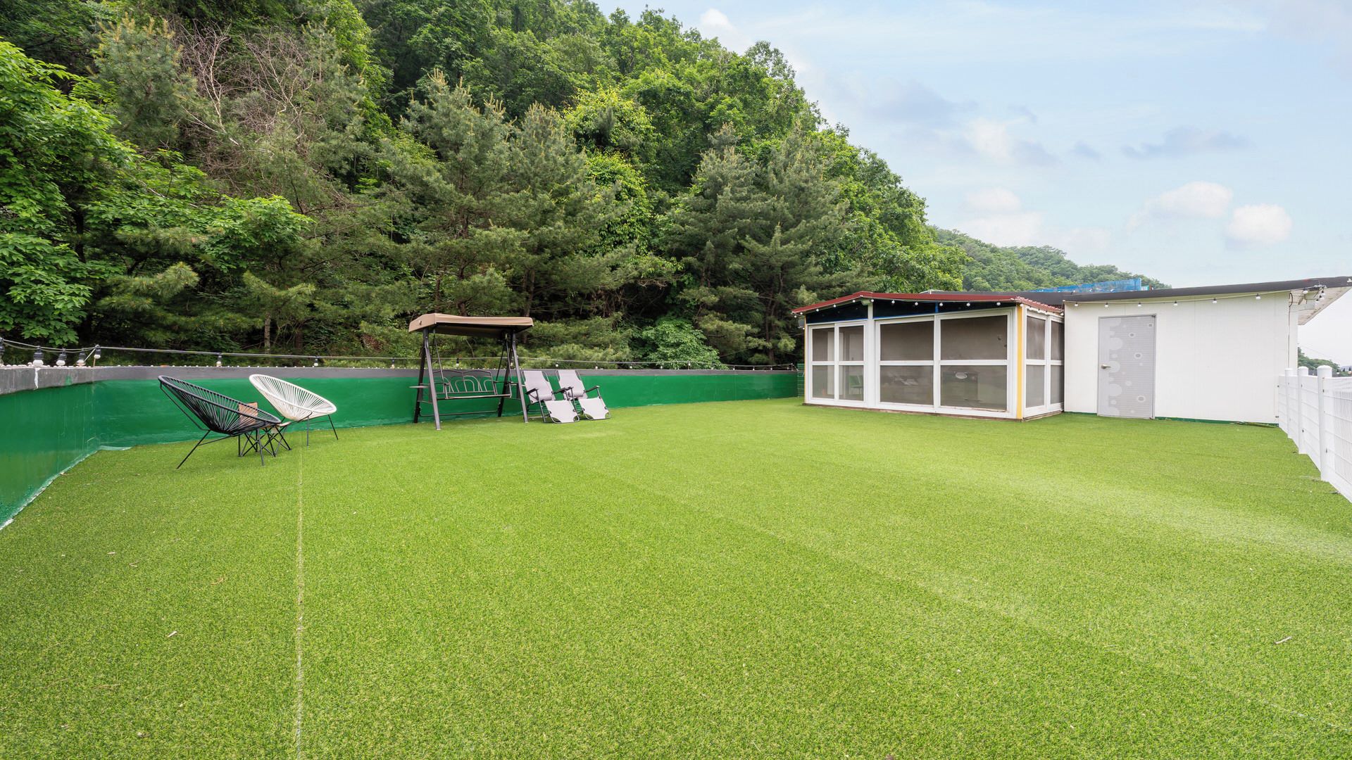 A grassy outdoor area with a swing set, a covered seating area, and a building with large windows.