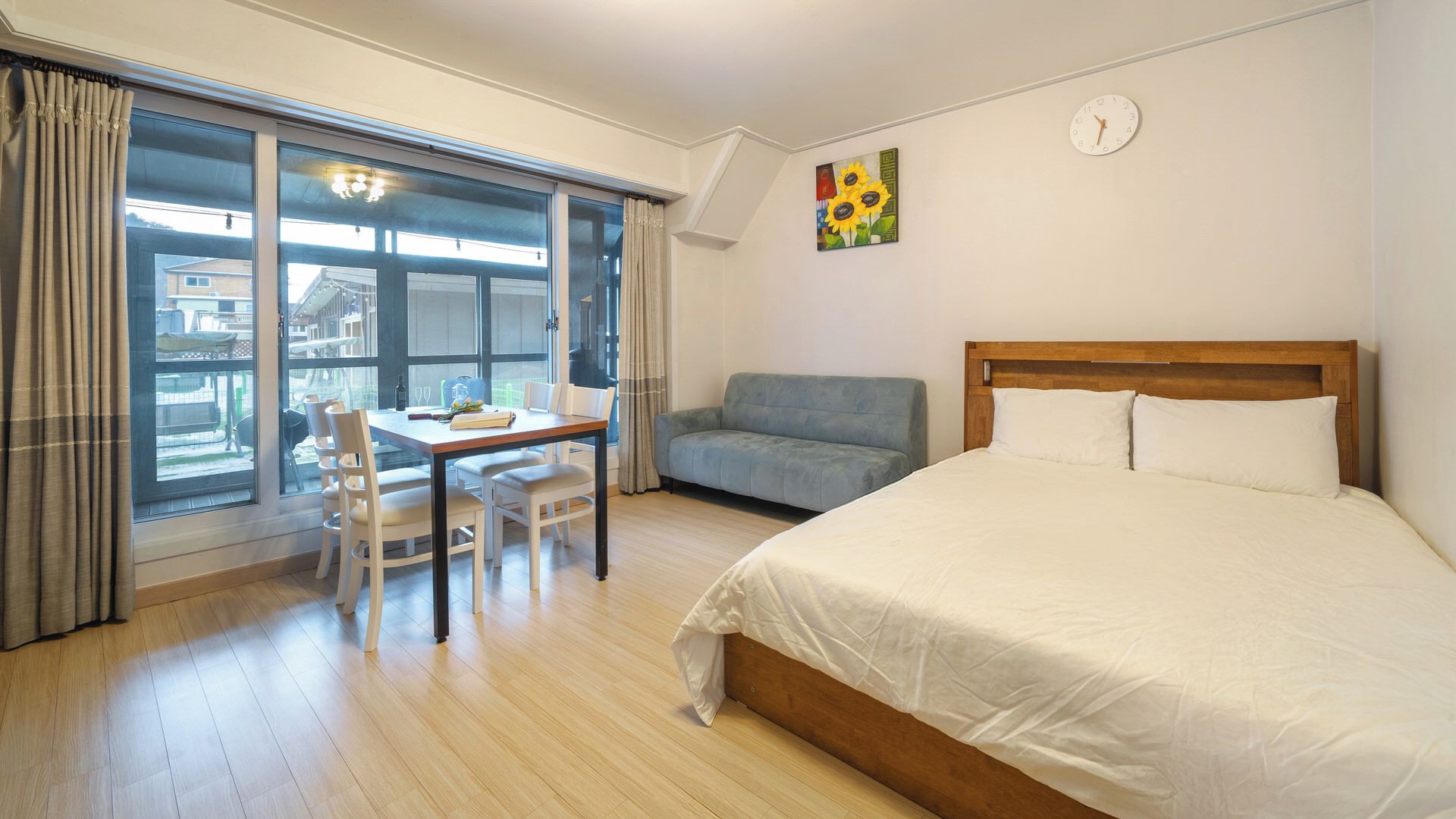 Ett hotellrum med en säng, ett bord med stolar, en soffa, ett stort fönster och en väggklocka.