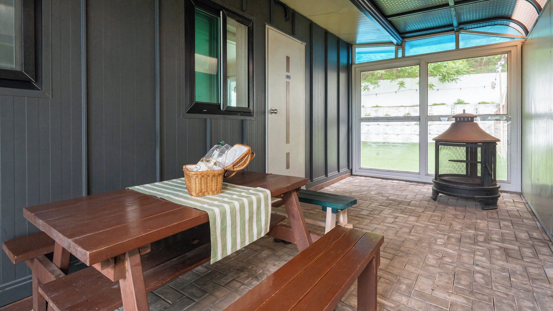 A covered outdoor seating area with a wooden table and benches, a wicker basket, and a lantern.