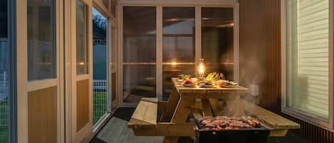 An outdoor patio with a wooden table and grill, surrounded by glass doors and windows.