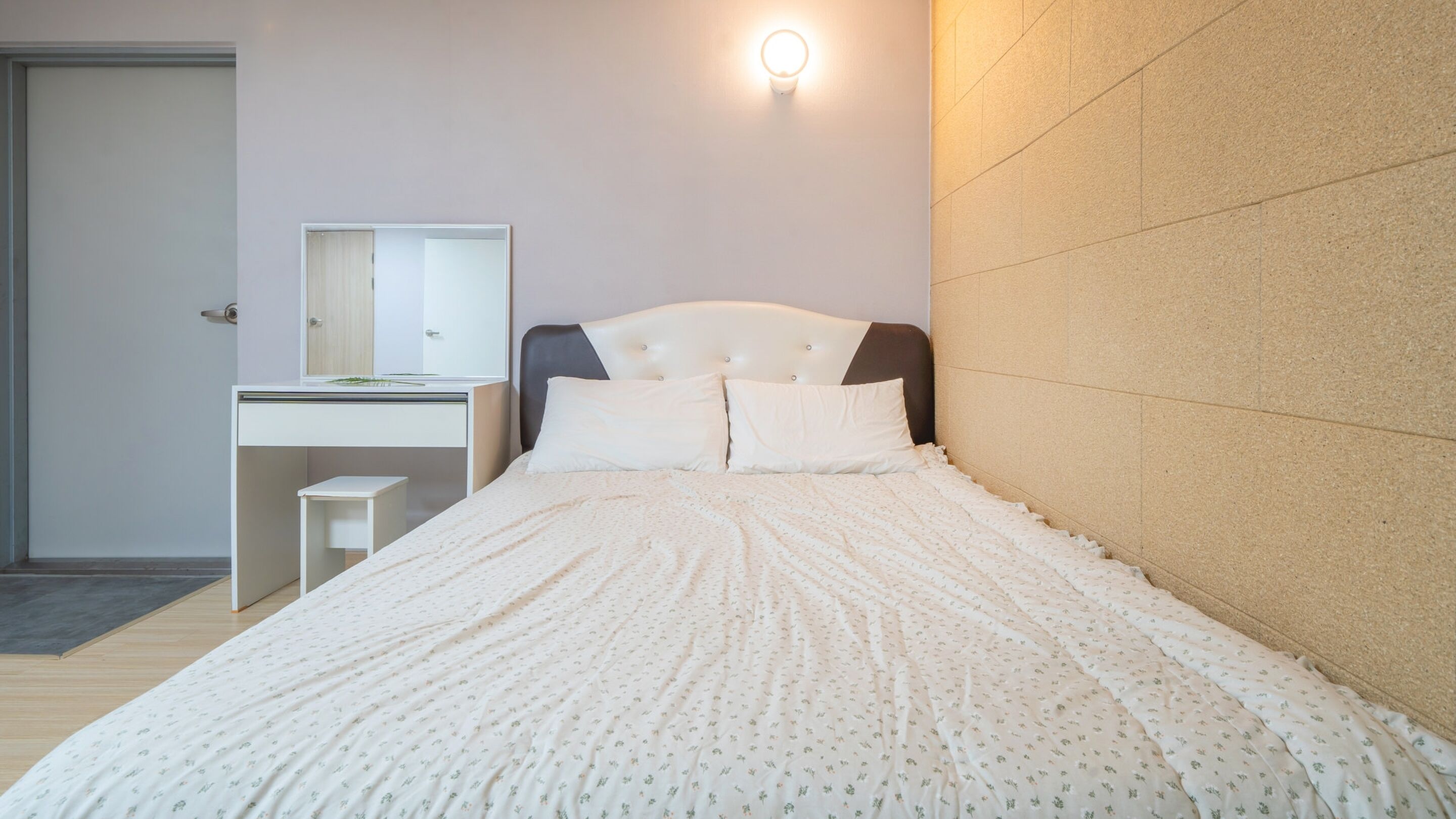 A bedroom with a bed, a bedside table, a mirror, and a wall-mounted light.