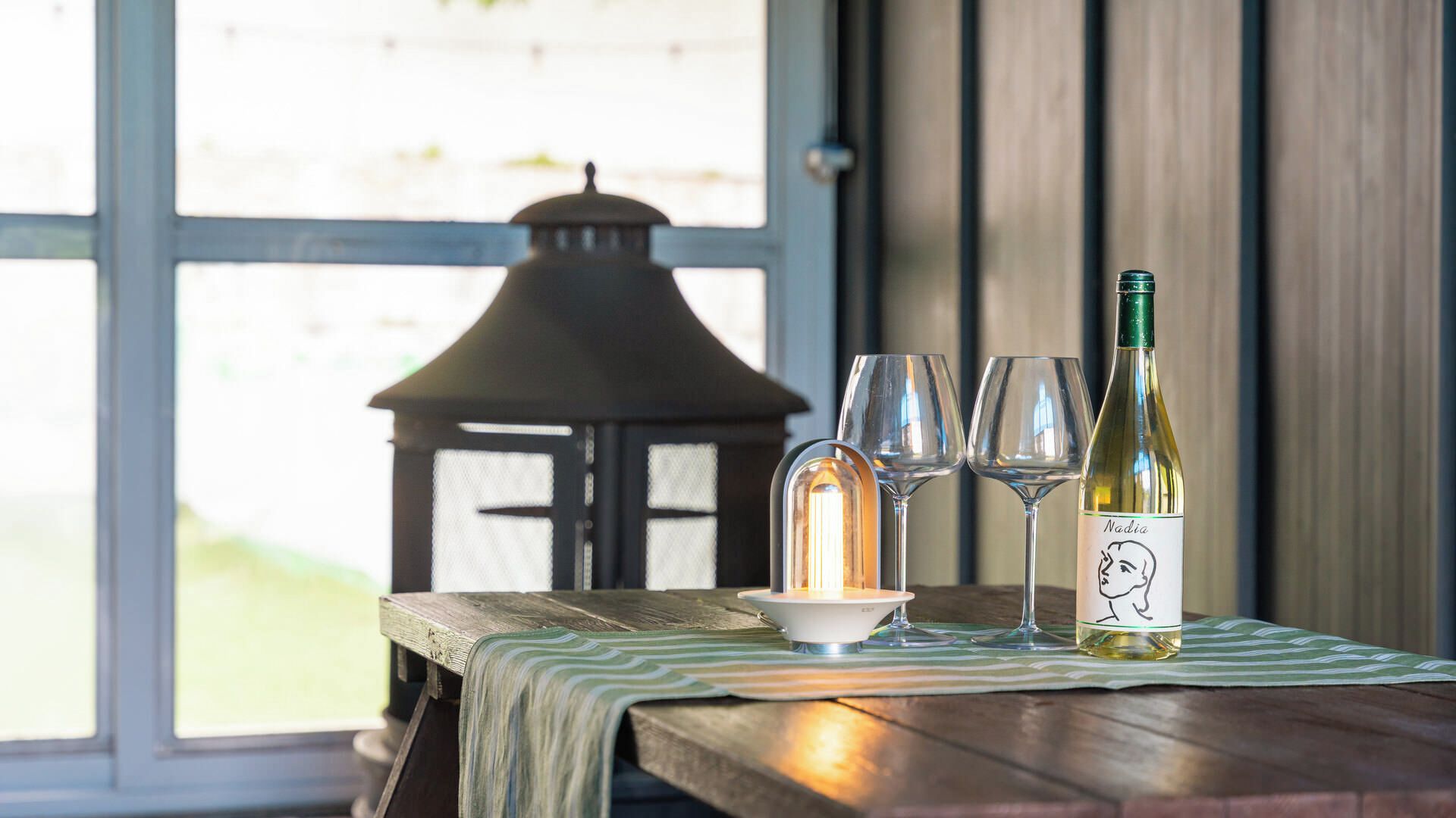 A table with a bottle of wine, two glasses, and a candle on a tablecloth.