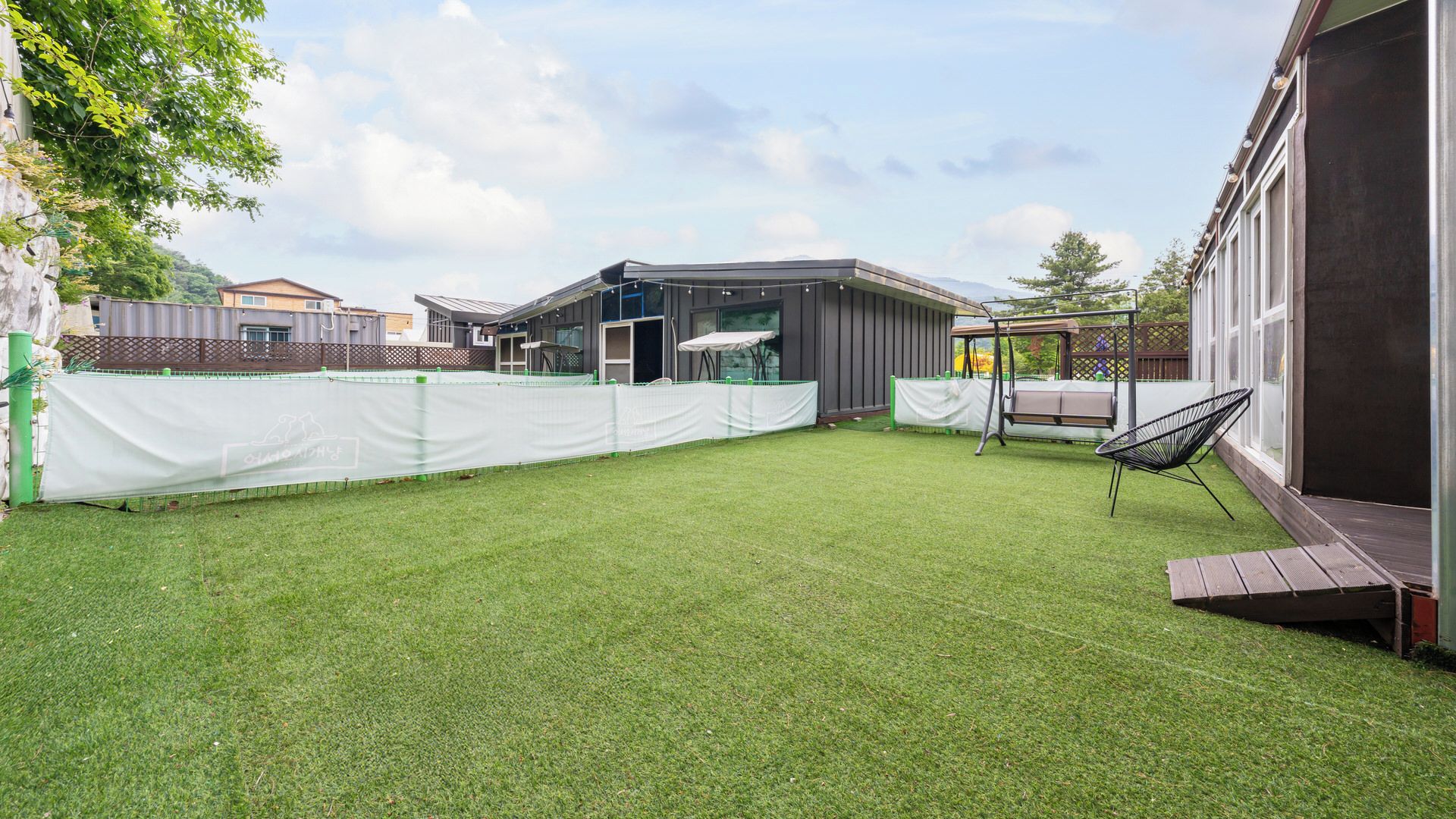 A well-maintained backyard with artificial grass, a swing set, and a covered seating area.