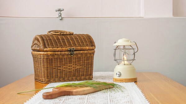 A wicker basket and a white lantern on a wooden table with a white cloth.
