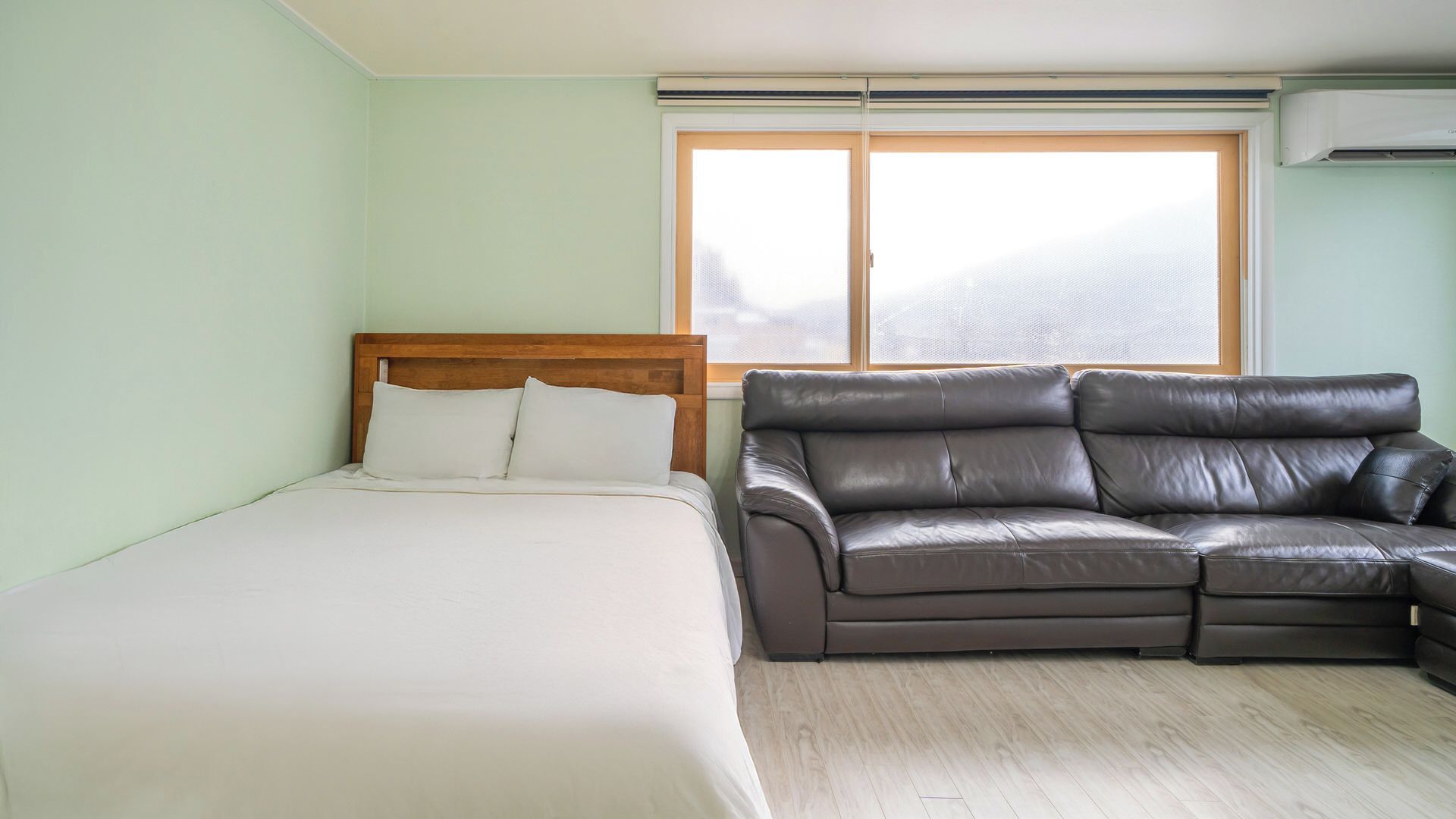 Een slaapkamer met een bed, een leren bank, een raam met zonwering en een airconditioning.