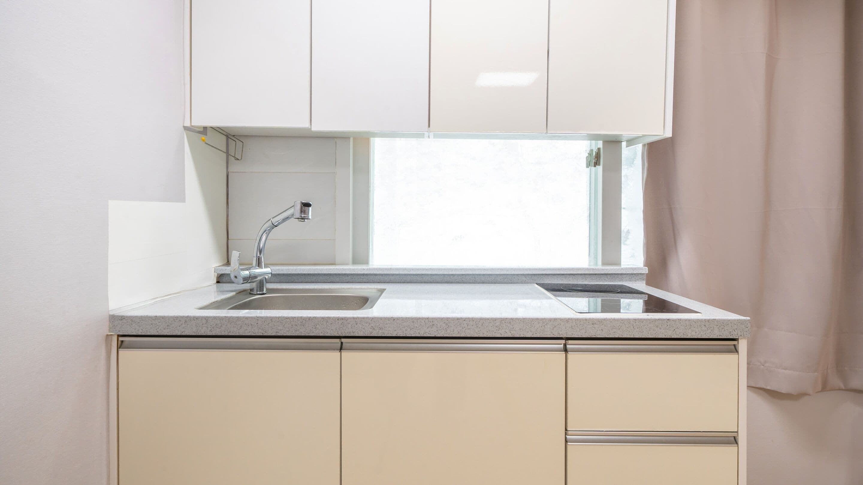 A kitchen with a stainless steel sink, a window above the sink, and beige cabinets.
