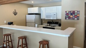 A kitchen with white cabinets, a microwave, a refrigerator, a coffee machine, and a bar stool. - Two Bedroom, Two Bath Condo ready for year-around fun. Great Up North Getaway! (Bellaire)