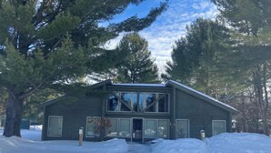 A two-story house with large windows, a garage, and a snow-covered driveway. - Two Bedroom, Two Bath Condo ready for year-around fun. Great Up North Getaway! (Bellaire)