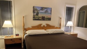 A neatly made bed with a wooden headboard, two bedside lamps, a nightstand, and a painting of a lakeside scene on the wall. - Two Bedroom, Two Bath Condo ready for year-around fun. Great Up North Getaway! (Bellaire)