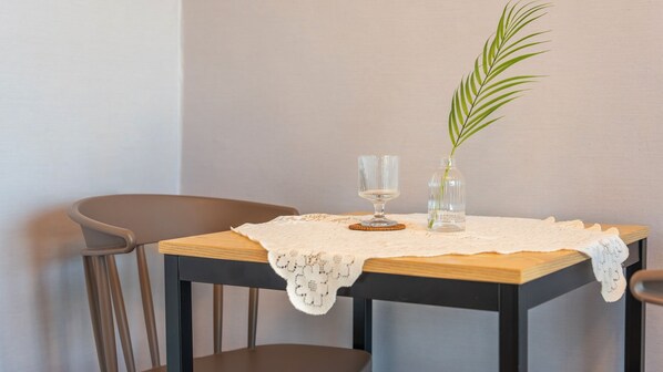 A table with a lace tablecloth, a clear glass, a glass vase with a plant, and a wooden coaster. - Sokcho Scenic House Pension (Sokcho)