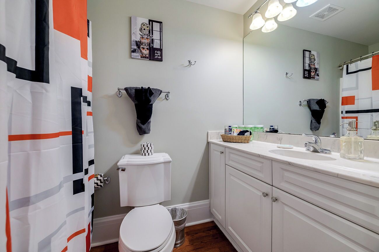 Un baño con inodoro blanco, lavamanos con espejo y cortina de ducha con estampado geométrico.