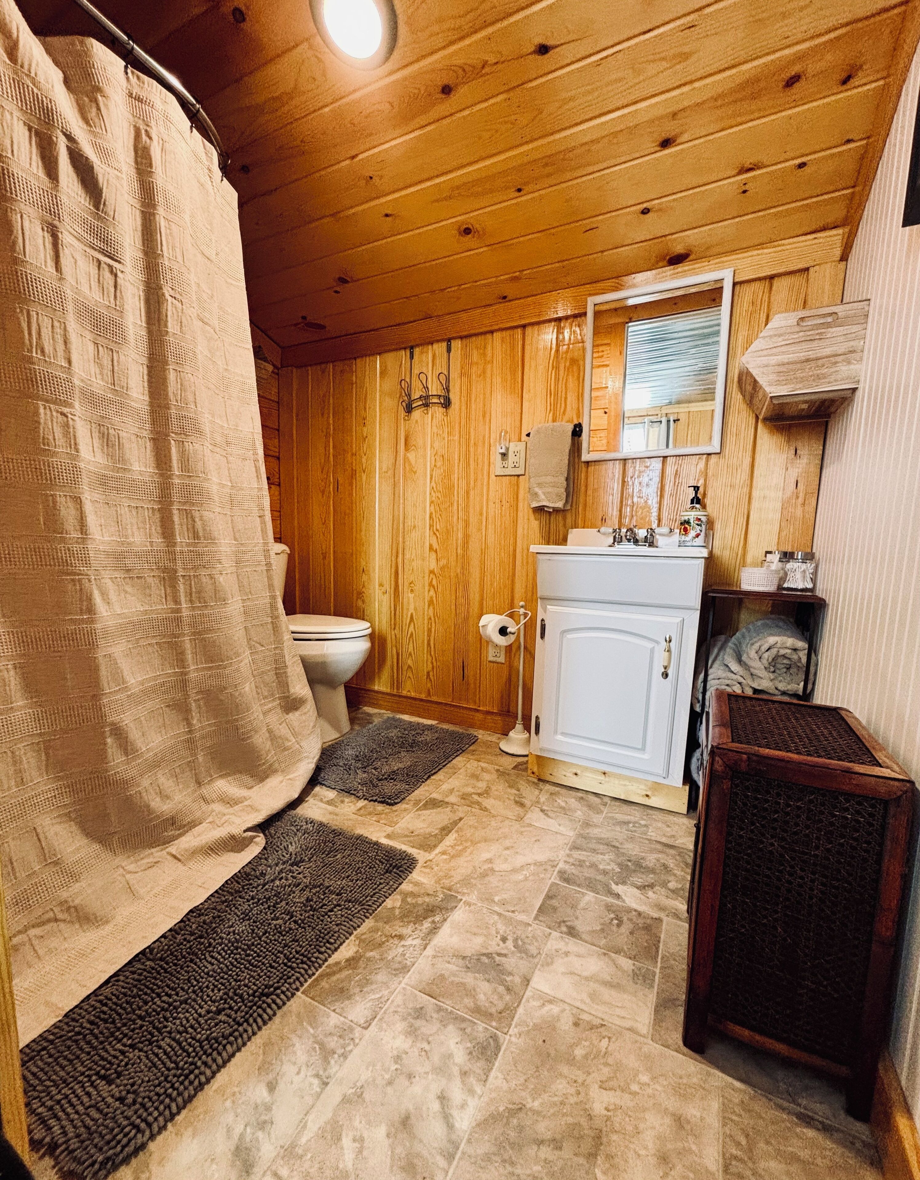 Une salle de bain aux murs lambrissés, équipée de toilettes, d’un lavabo et d’un espace douche.