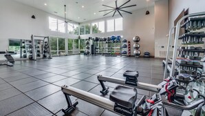 Een ruime fitnessruimte met diverse trainingsapparaten, grote ramen en een hoge plafond.