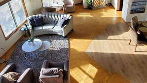 Een ruime loft met een hoge plafond, grote ramen, een gebogen hoekbank en een kleine ronde tafel.