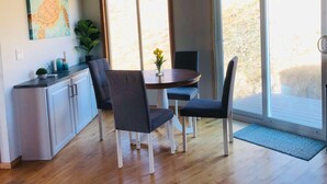 Een eetgedeelte met een tafel en stoelen, een schilderij aan de muur en een glazen schuifdeur naar een buitenruimte.