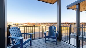 A balcony with two Adirondack chairs, a wooden ceiling, and a view of a parking lot and buildings. - Charming 3 bed townhome w/direct access to downtown GJ! NO EXTRA FEES! (Grand Junction)